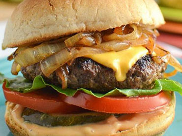 Delicious-looking cheeseburger with grilled onions, lettuce, tomato and pickle on a toasted bun shown on a dark, teal plate